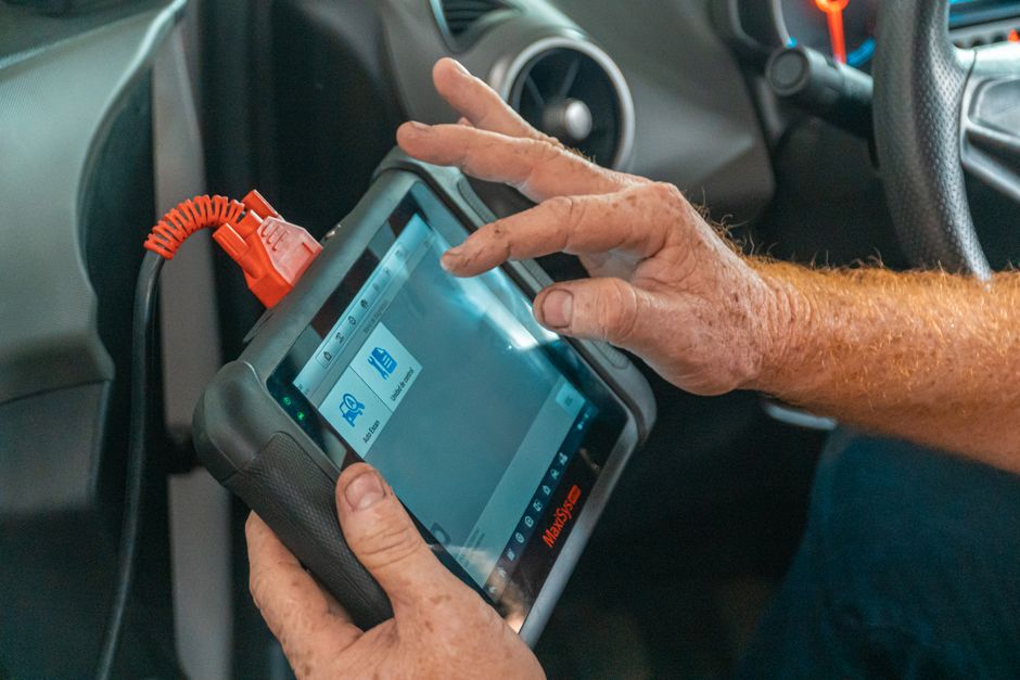 Mechanic using a diagnostic tool inside a car to check for engine issues and ensure proper maintenance.